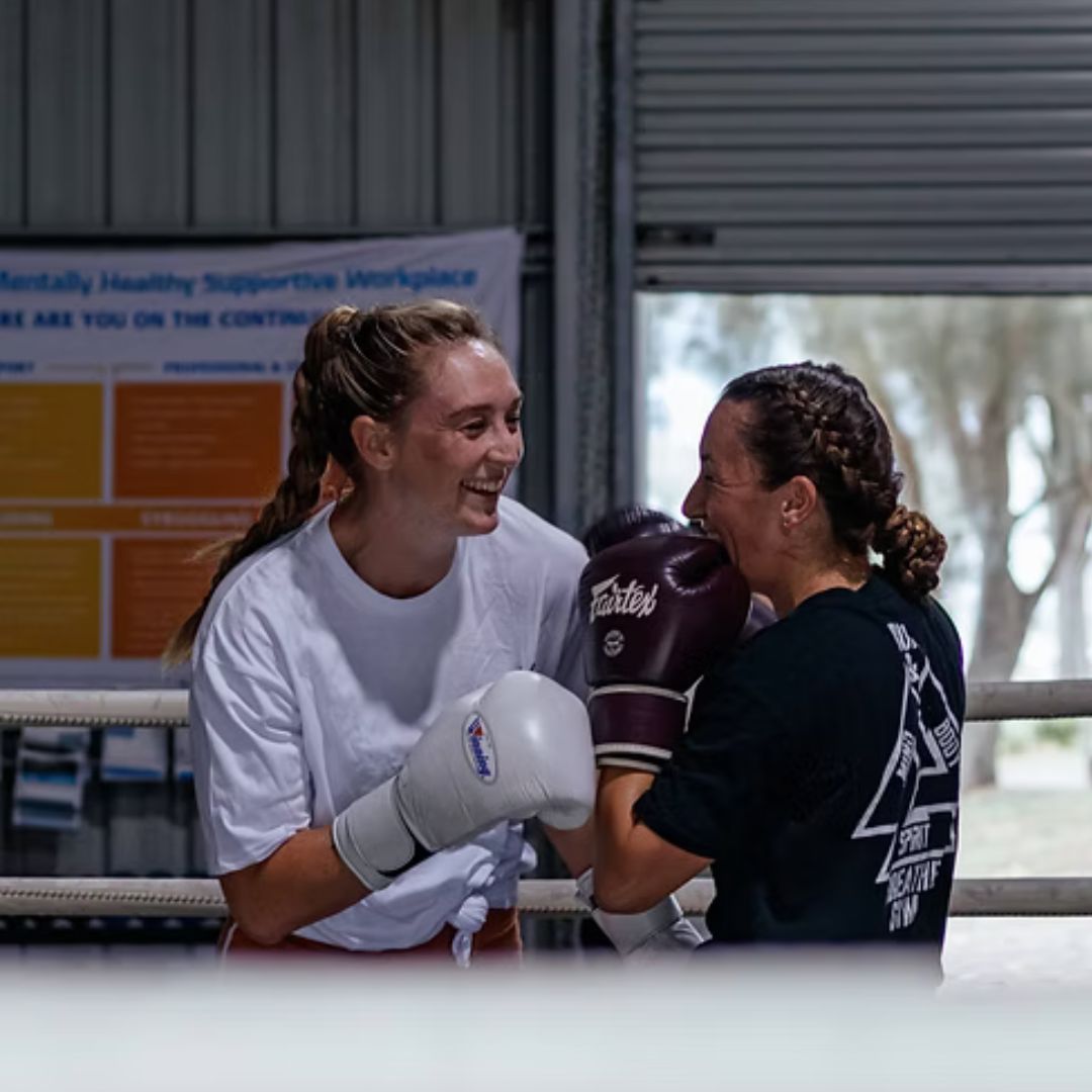 Two women laughing together in the ring during pad work