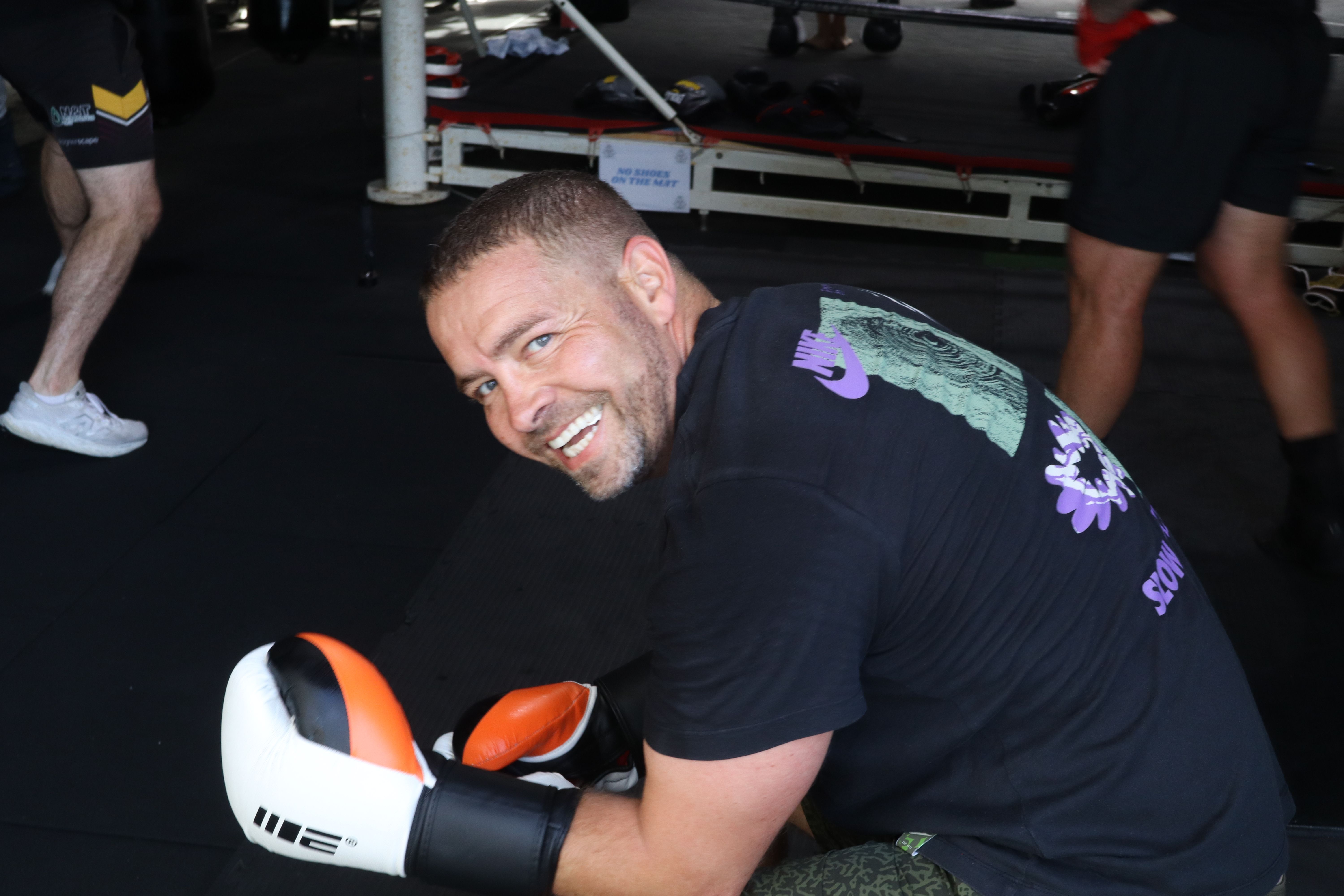 Peter crouching and smiling in orange and white gloves on the mat